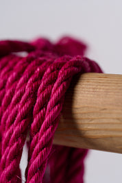 Macro pink jute rope hanging over wooden rod on white background.