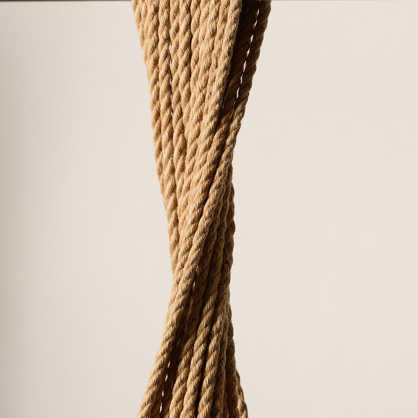 A close-up of a 6mm, twisted tan jute, rope hanging from a horizontal metal rod against a plain beige background.
