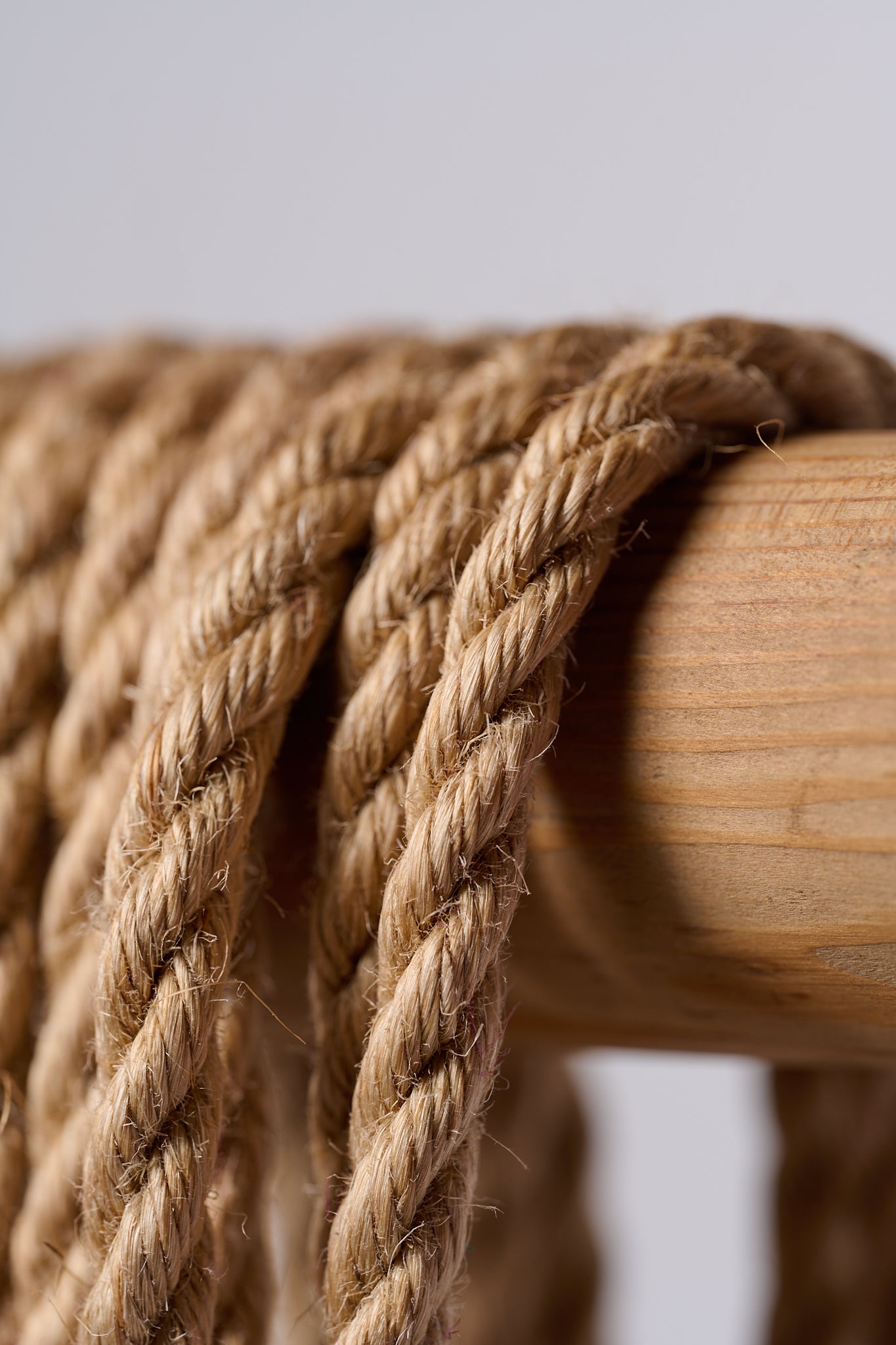 Macro natural jute rope hanging over wooden rod on white background.