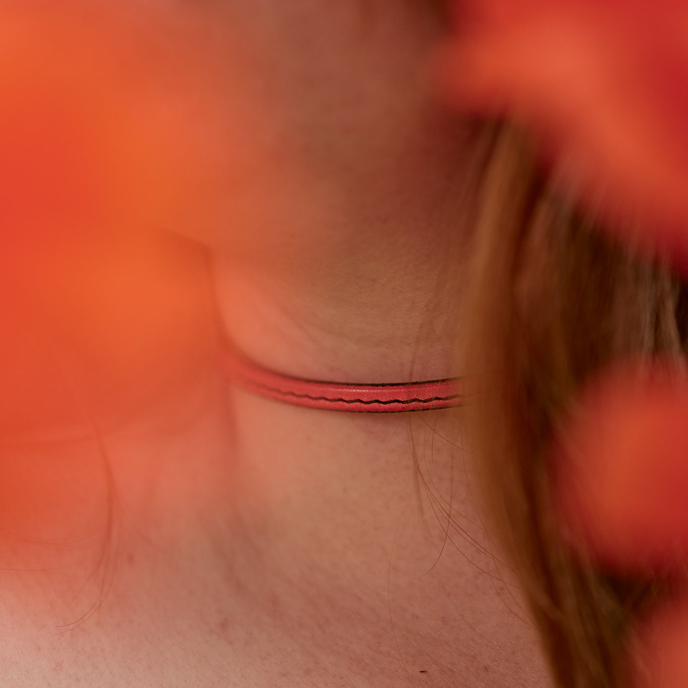 Close-up of a person's neck with a thin red necklace, surrounded by blurred orange flowers.