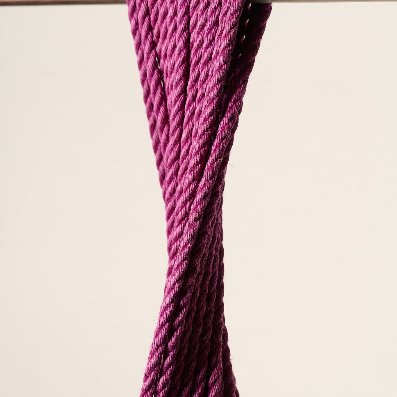 A close-up of a thick, twisted, purple, jute rope draped over a horizontal metal rod against a plain beige background.