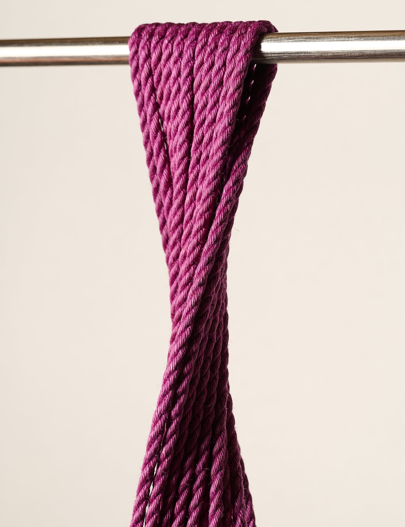 A close-up of a thick, twisted, purple, jute rope draped over a horizontal metal rod against a plain beige background.