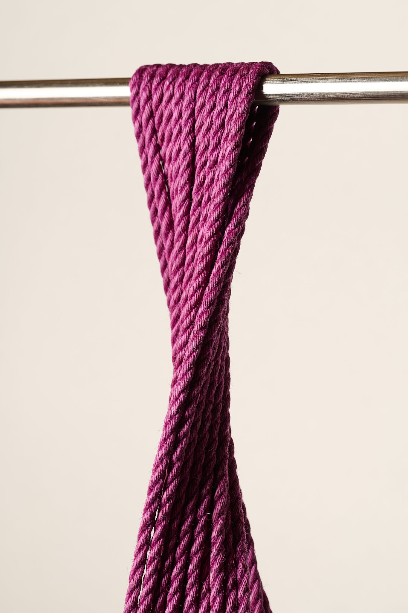 A close-up of a thick, twisted, purple, jute rope draped over a horizontal metal rod against a plain beige background.