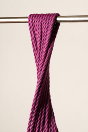 A close-up of a thick, twisted, purple, jute rope draped over a horizontal metal rod against a plain beige background.