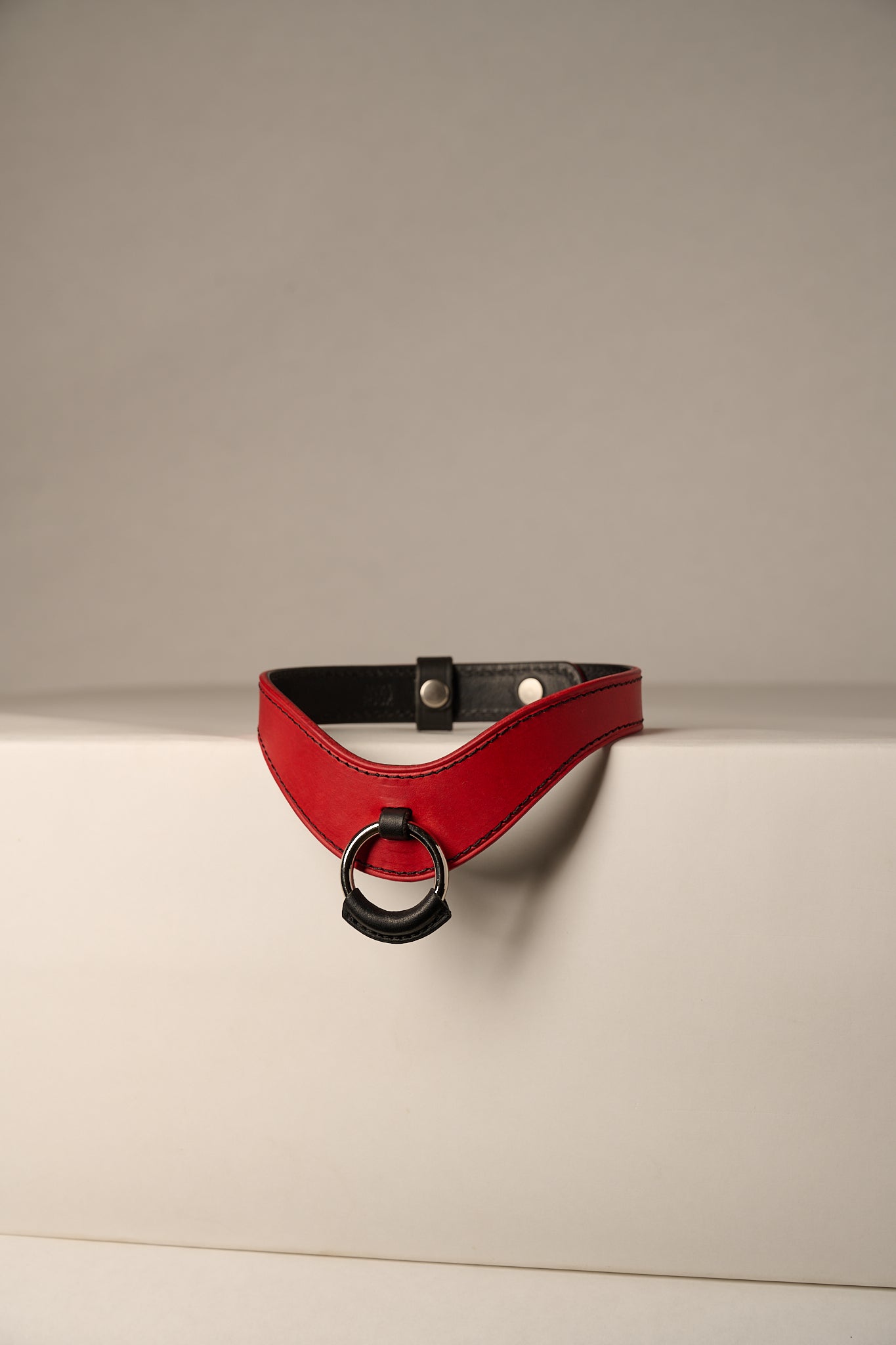 red and black leather necklace with a ring on a beige background