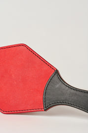 Macro shot of  red leather paddle with a black handle, showing a semi-stiff construction and black stitching.