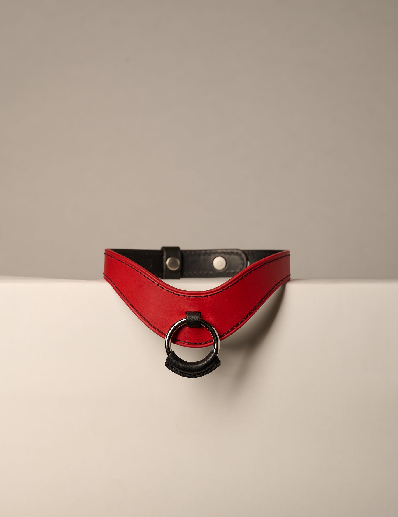 red and black leather necklace with a ring on a beige background