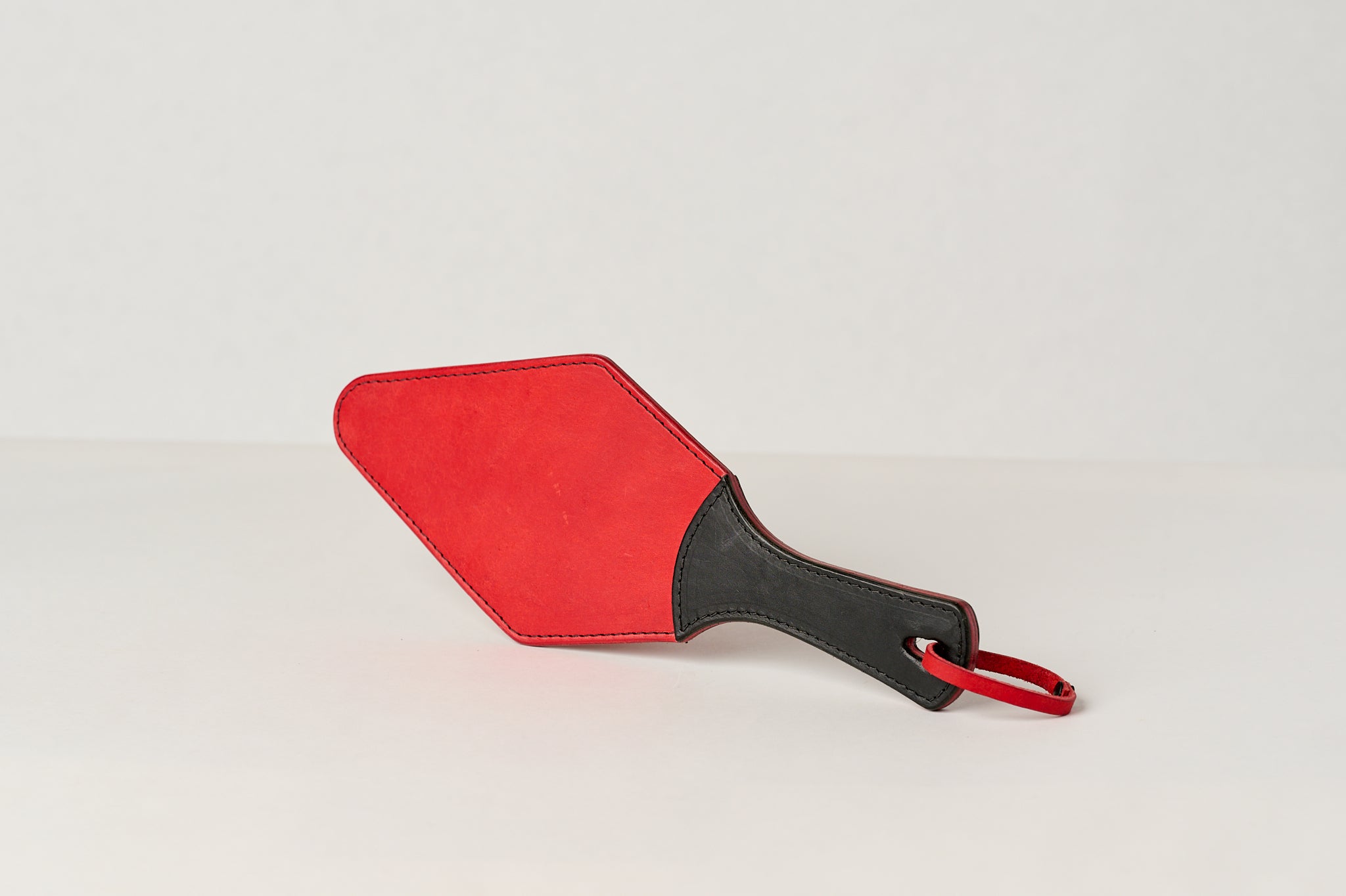 A red leather paddle with a black handle, showing a semi-stiff construction.