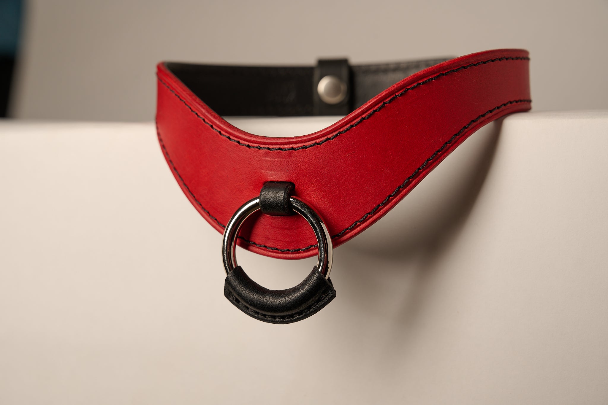 red and black leather necklace with a ring on a beige background
