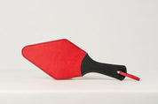 A red leather paddle with a black handle, showing a semi-stiff construction.