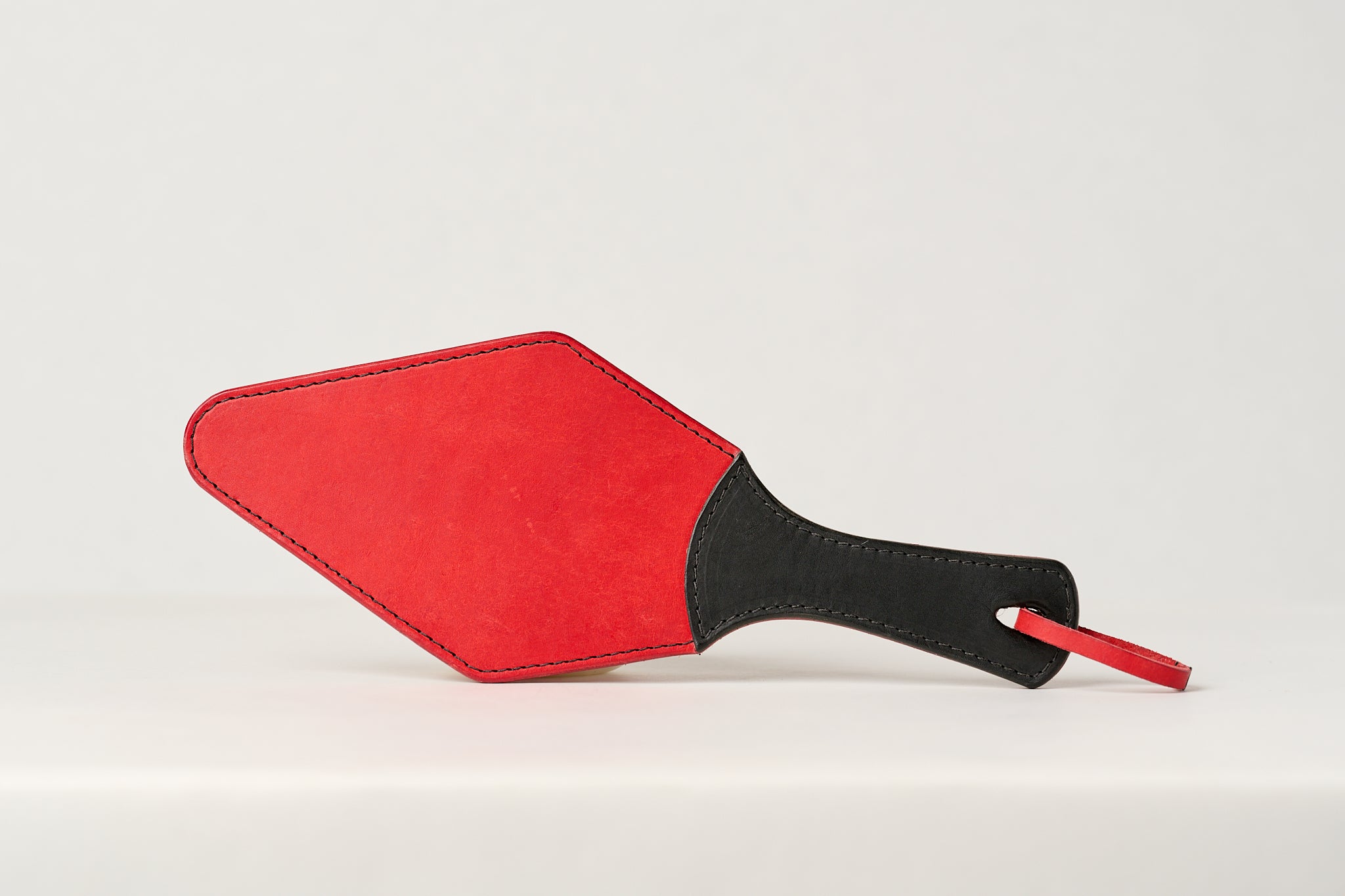 A red leather paddle with a black handle, showing a semi-stiff construction.