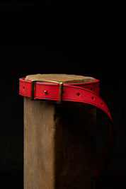 red leather belt strapped around wood post on black background