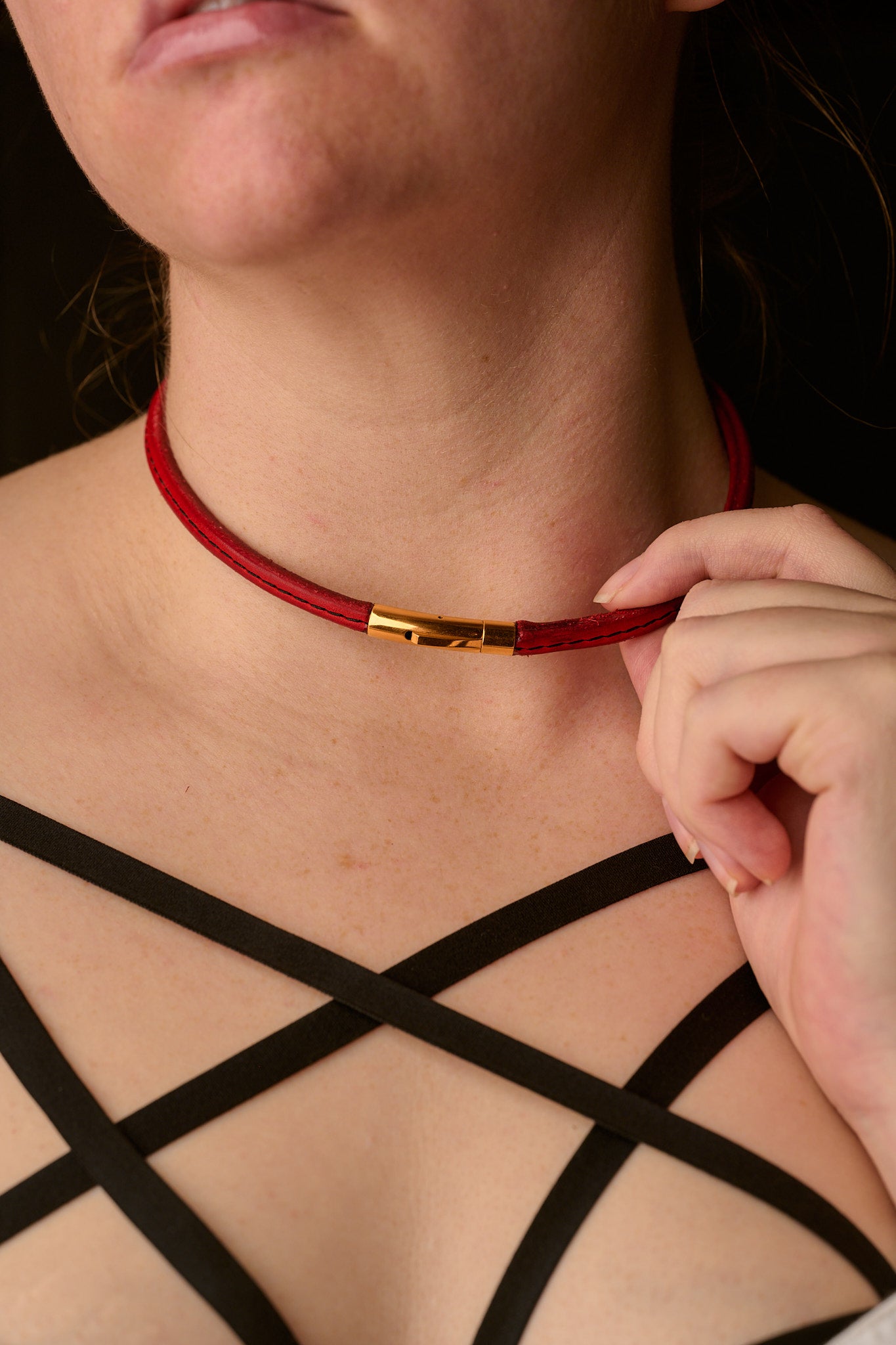 Person wearing a red choker with a gold clasp, adjusting it with their hand.