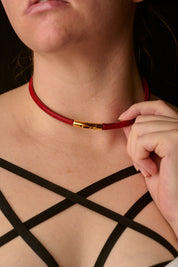 Person wearing a red choker with a gold clasp, adjusting it with their hand.