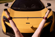 woman's legs in anklets attached to adjustable silver bar in front of McLaren