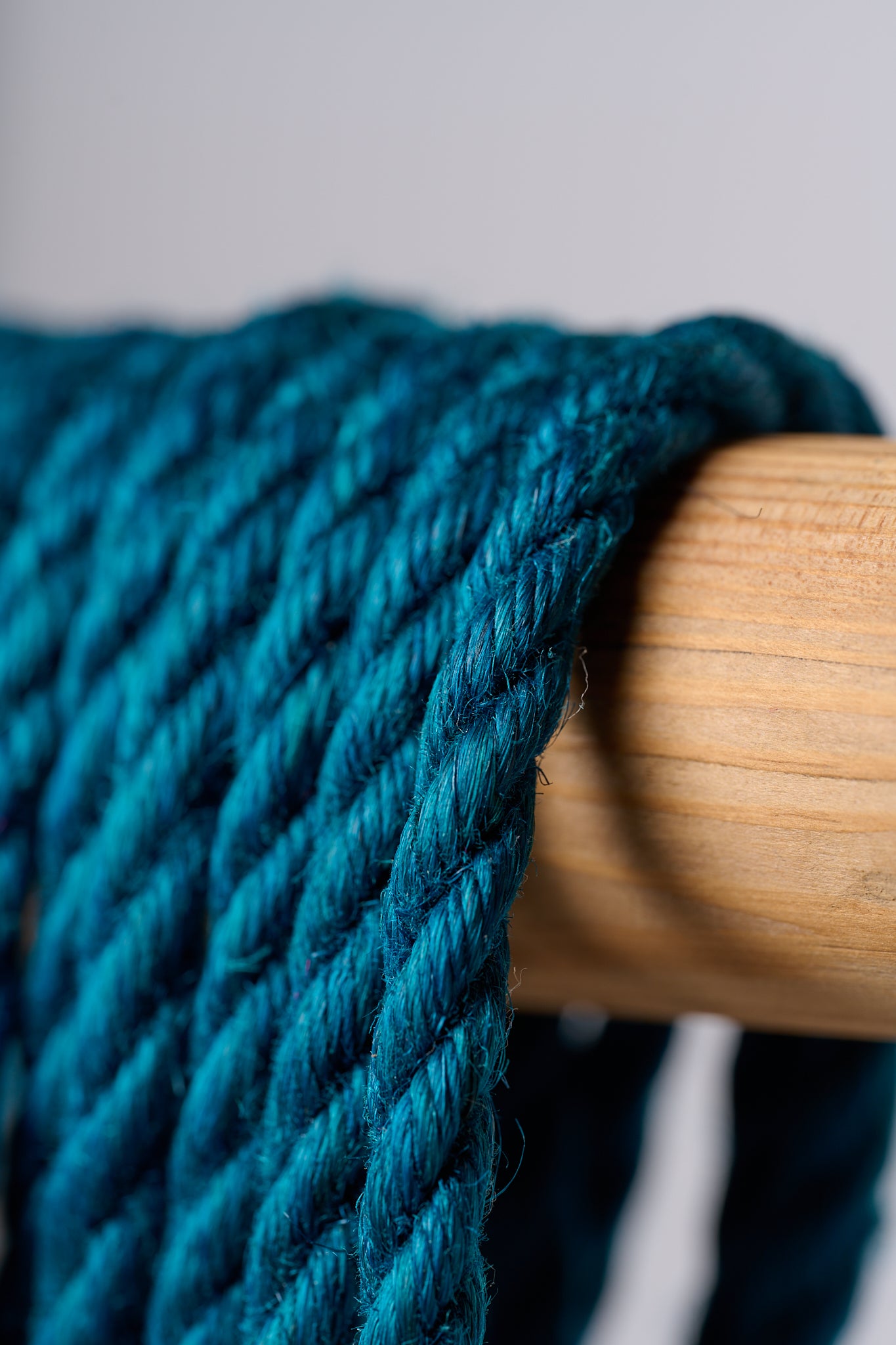 Macro blue jute rope hanging over wooden rod on white background.