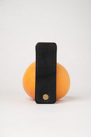 foldable black  leather travel size belt with rivets on white background with grapefruit behind.