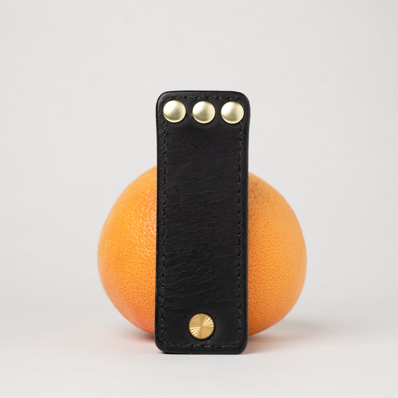 foldable black  leather travel size belt with rivets on white background with grapefruit behind.