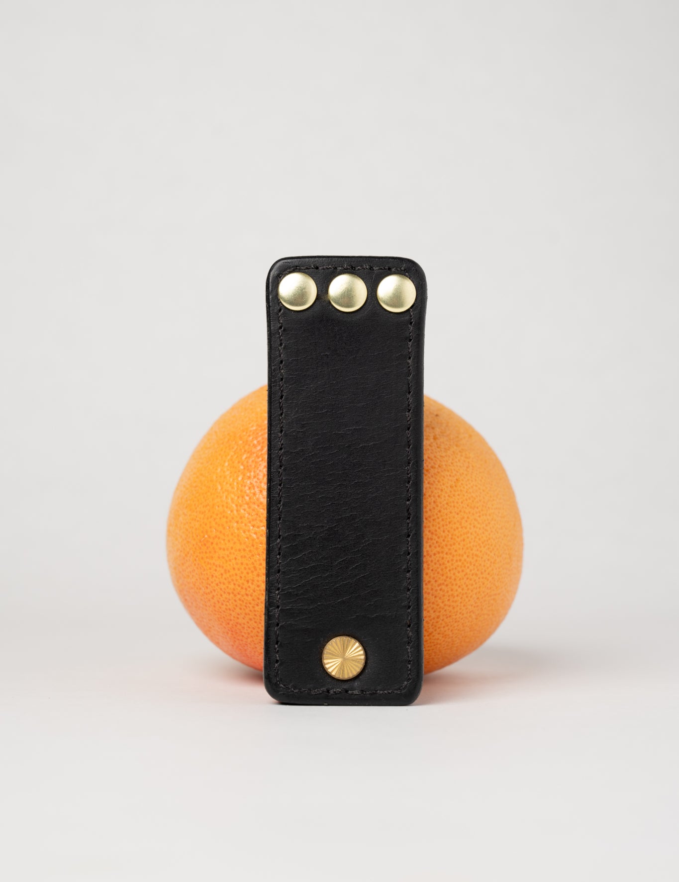 foldable black  leather travel size belt with rivets on white background with grapefruit behind.